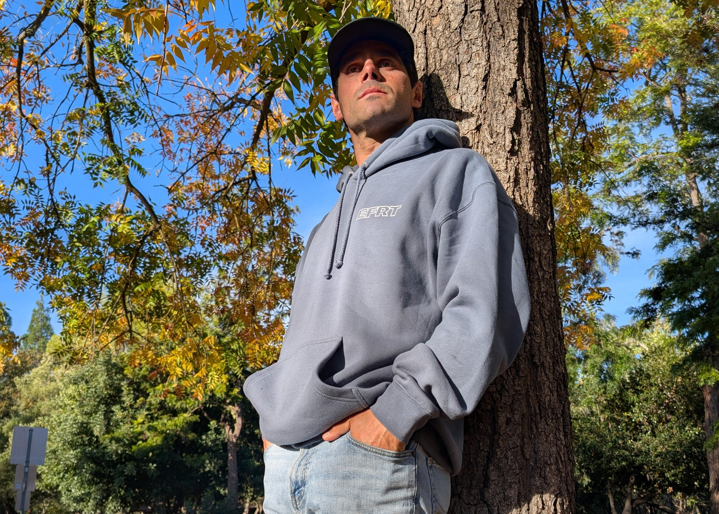 Man leaning against a tree in a park with autumn leaves