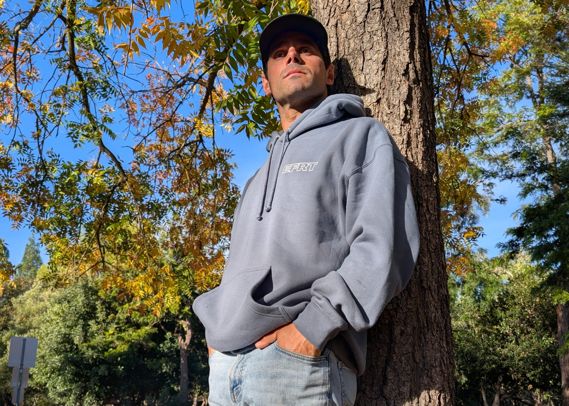 Man leaning against a tree in a park with autumn leaves